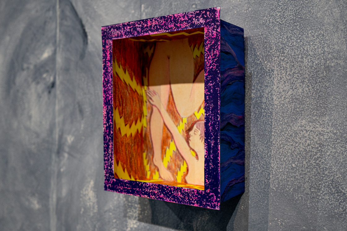 a small cardboard box is hanging on a grey wall. inside there is a drawing of a girl. her top half is coming from the bottom of the box and her bottom half is climbing up inside the box. the colours are purple and fluorescent yellow.