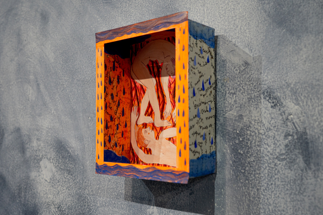 a small cardboard box hanging on a grey wall. there is a drawing of a boy and a girl inside the box being cramped in a small space. there are raindrops on the inside walls of the box as well as on the outside. the colours are blue and orange.